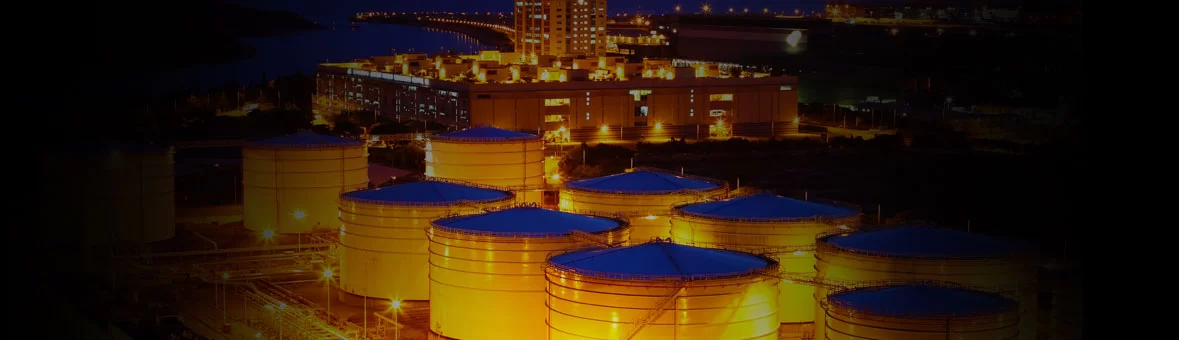 Tanques de armazenamento iluminados em refinaria de petróleo à noite, representando a infraestrutura da indústria de óleo e gás
